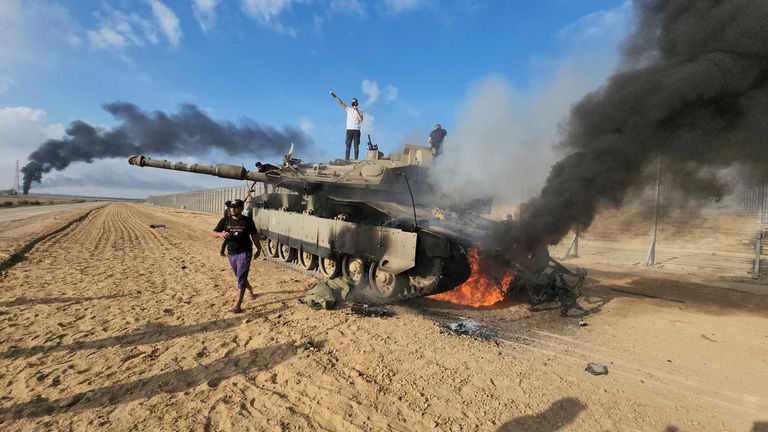 Palestinians celebrate by a destroyed Israeli tank at the Gaza Strip fence east of Khan Younis southern Saturday, Oct. 7, 2023. The militant Hamas rulers of the Gaza Strip carried out an unprecedented, multi-front attack on Israel at daybreak Saturday, firing thousands of rockets as dozens of Hamas fighters infiltrated the heavily fortified border in several locations by air, land, and sea and catching the country off-guard on a major holiday. (AP Photo/Hassan Eslaiah)